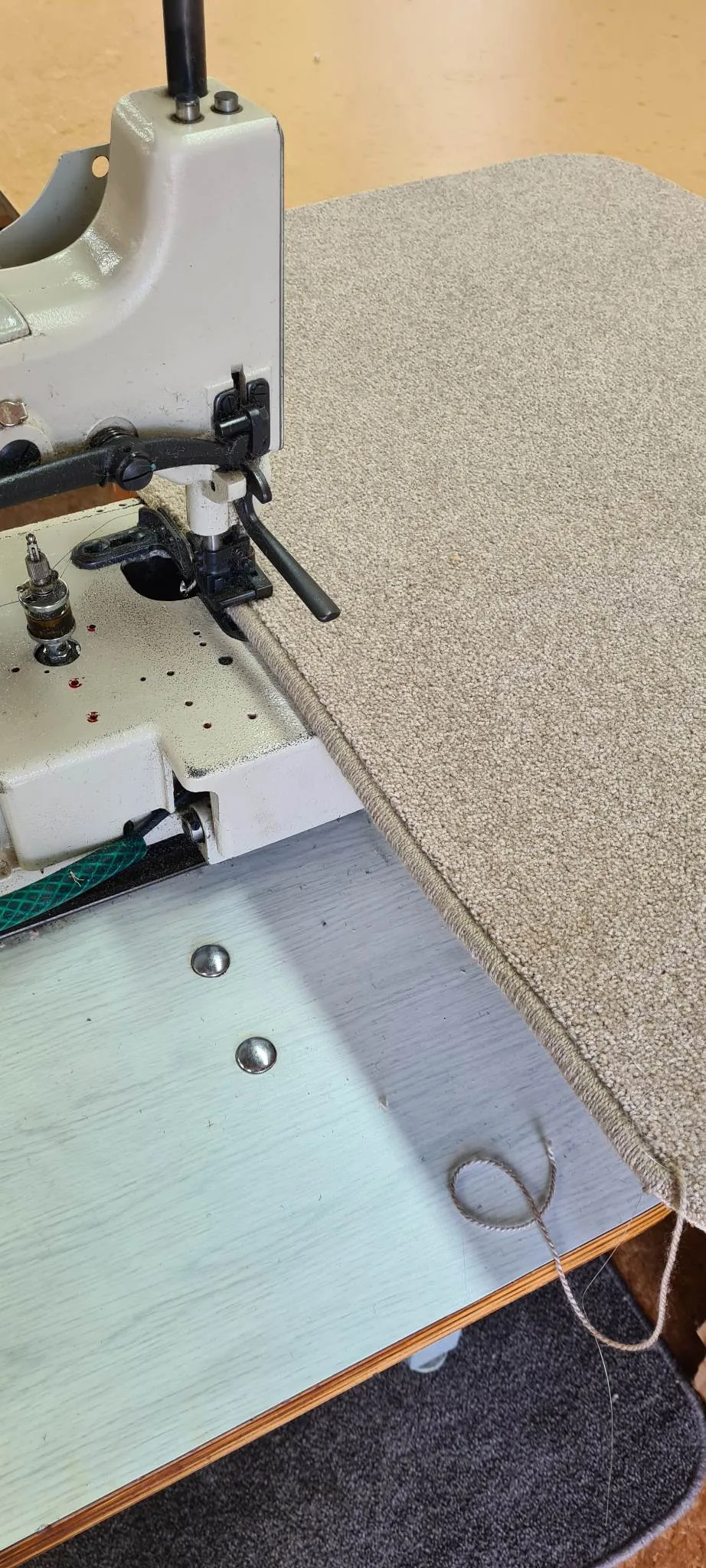 Close-up of industrial carpet overlocking machine stitching a beige carpet edge