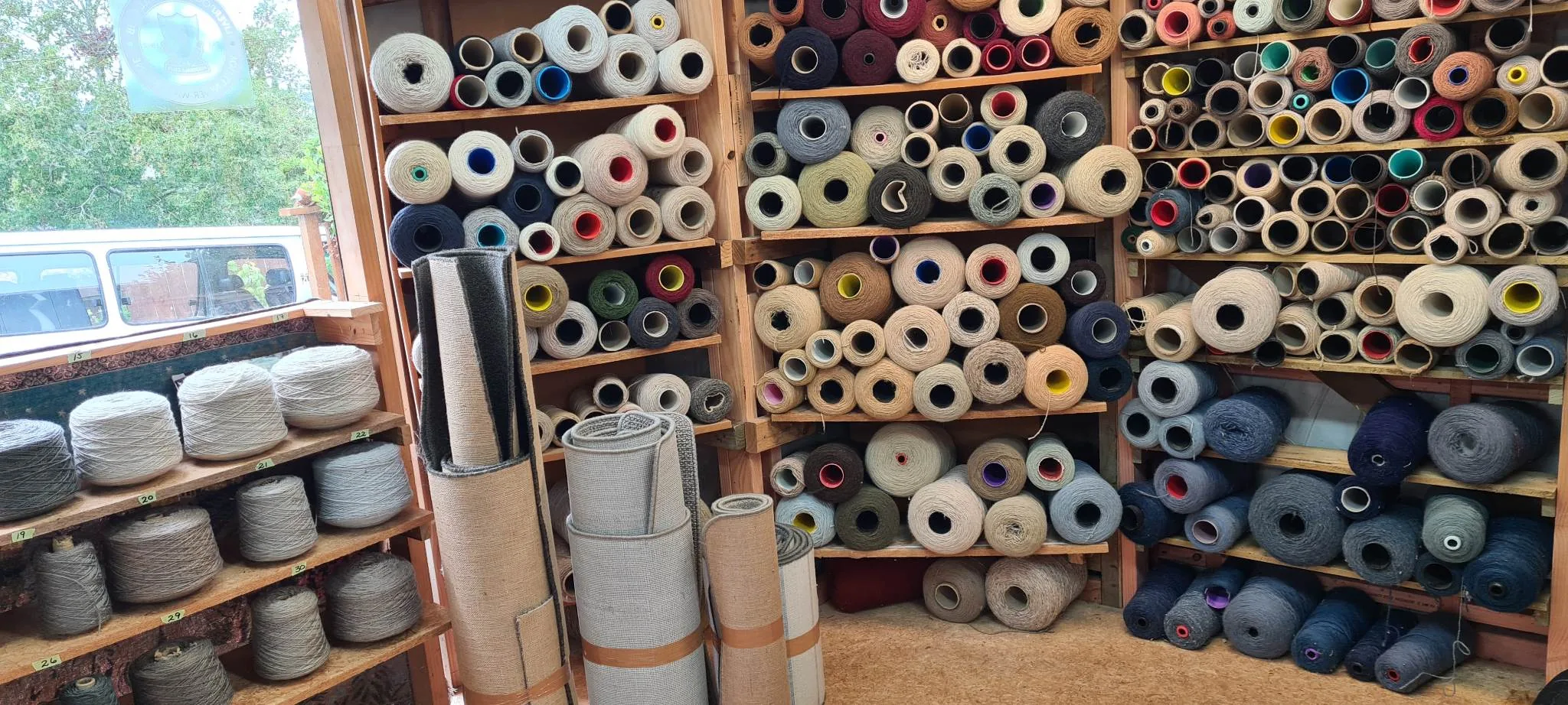 Carpet overlocking workshop with yarn wall and finished carpet rolls